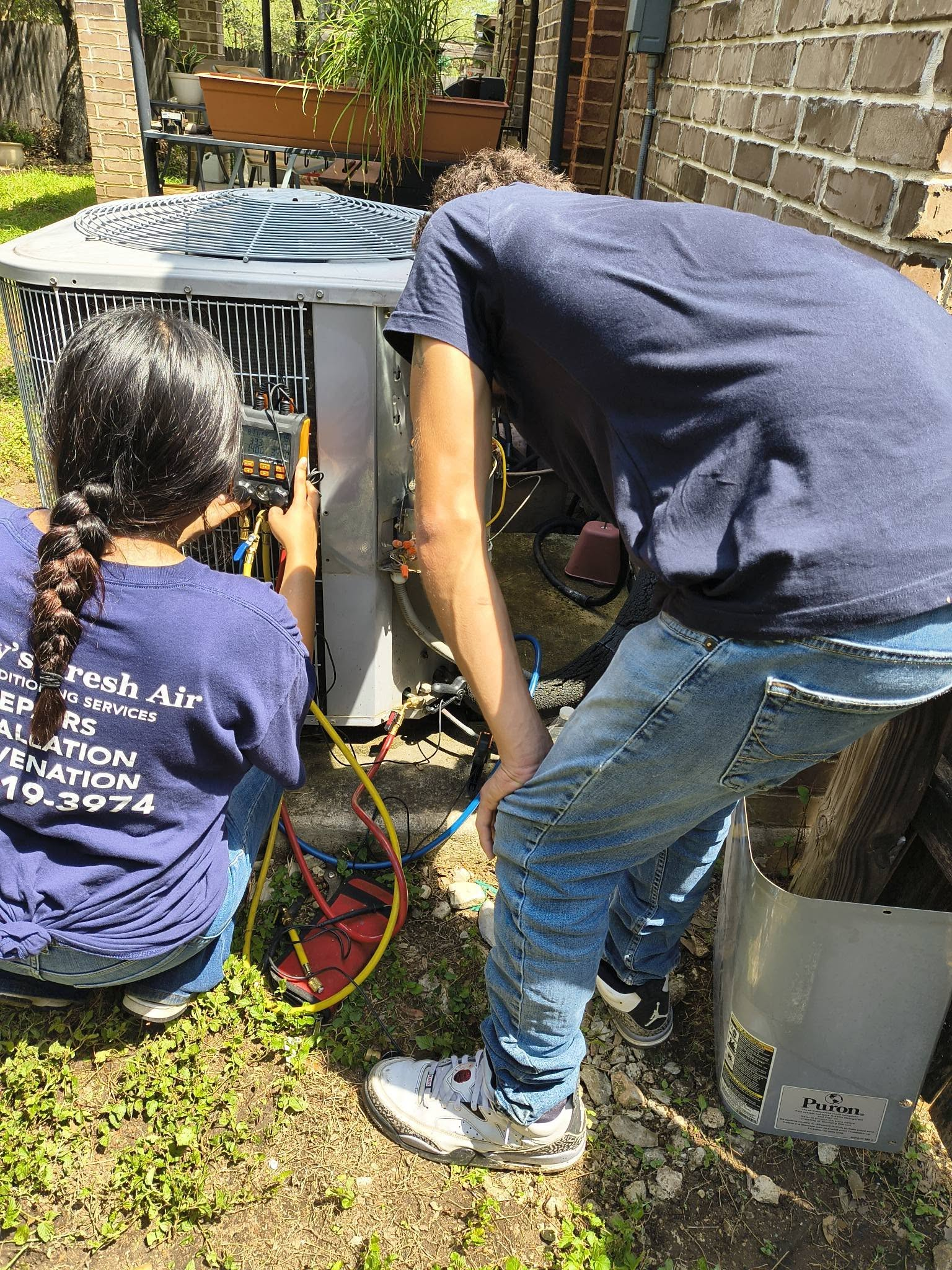 Two technicians checking gauges on an outdoor unit